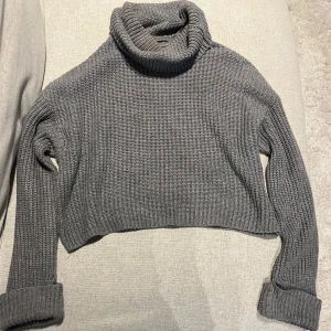 Grå stickad polotröja från Housebrand - Säljer en mysig grå stickad polotröja från Housebrand. Tröjan är croppad med långa ärmar och har en hög polokrage. Perfekt för kyliga dagar!