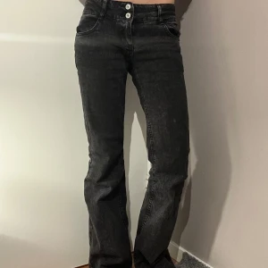 Svarta jeans med knappar - Snygga svarta jeans med hög midja och två knappar framtill. De har en straight passform och är perfekta för en stilren look. Jeansen har en klassisk design med fickor både fram och bak.