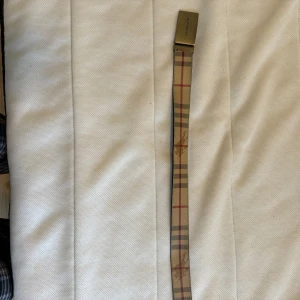 bälte från Burberry - Snyggt bälte från Burberry med klassiskt rutigt mönster i beige, rött och svart. Bältet har ett stilrent spänne i silverfärg och kommer i originalförpackning med tillhörande påse. Perfekt för att ge en touch av lyx till din outfit.