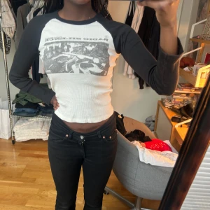 Vit och svart långärmad croppad topp - Säljer en vit och svart långärmad topp med tryck framtill. Toppen är croppad och har en kontrasterande design med svarta ärmar och vit kropp. 