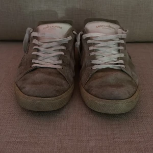 Saint Laurent skor size 43 passar 44 - Snygga beige sneakers från Saint Laurent med vit snörning och texten 'Saint Laurent' på sidan. Skorna har en klassisk design med en bekväm sula och är perfekta för en stilren look. Har ni frågor är det bara höra av er priset går att diskutera vid snabb affär. Inget og medföljer!
