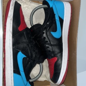 Nike Air Jordans i svart, röd och blå - Snygga Nike Air Jordans i en cool färgkombination av svart, röd och blå. Skorna har den klassiska Nike-loggan i blått på sidan och svart snörning. Perfekta för dig som vill ha en stilren och sportig look.