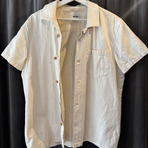Vit/beige kortärmad skjorta från Weekday - Säljer en stilren vit/beige kortärmad skjorta från Weekday. Skjortan har en klassisk krage och knappar framtill. 
