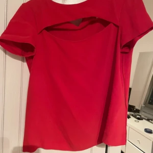 Röd blus från Maje - Säljer en snygg röd topp från Maje med korta ärmar och en unik design med öppning vid halsen. Jättebra skick och i strl 1 som motsvarar s