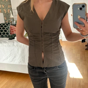 Brun korsettliknande topp  - Snygg brun korsettliknande topp med knappar framtill. Den har en v-ringad design och är ärmlös. Från weekday, använt max 2 ggr 