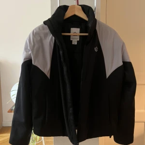Svart och grå jacka från Adidas - En adidasjacka, croppad, svart och grå. Bra skick med bra kvalité. Glansigt material men hyfsad fodrad och varm. Snygg jacka som kommer passa nu till våren och även höst/vinter! Sitter snyggt. Passar till strl S - xs om du vill ha lite mer oversize. Har fickor, innerficka och går även att dra ihop nertill. Hör av dig vid frågor och priset går att pruta. 