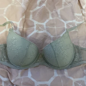 Grön spets-bh - Säljer en elegant grön bh med spetsdetaljer. Den har justerbara axelband och en mjuk kupa för extra komfort. Perfekt för att känna sig både bekväm och stilfull. 