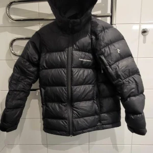 Svart pufferjacka från Peak Performance - Säljer en svart pufferjacka från Peak Performance. Jackan har en dragkedja framtill och en huva för extra skydd mot kyla. Jackan har några synliga hål men annars är den perfekt för kalla dagar med sin quiltade design som håller värmen inne. En stilren och funktionell jacka för vintern.