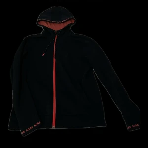Hugo boss tröja storlek (S/M) - Snygg svart hoodie med röda dragkedjor och snören. Perfekt för en avslappnad stil. Hoodien har en bekväm passform och är idealisk för kyligare dagar. Vid snabbaffär kan priset sänkas. Tröjan är i gott skick används fåtal  gånger bara. Bra passform och funkar som S och M.