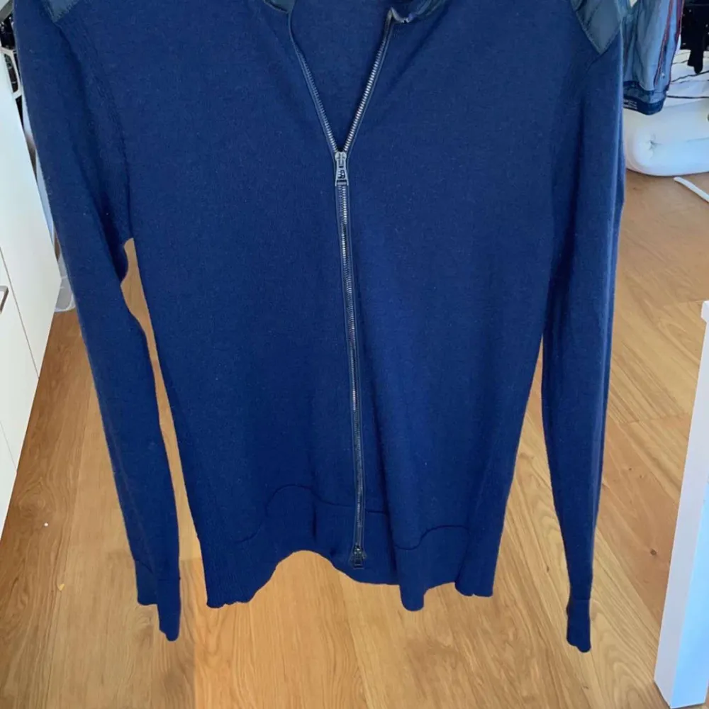 Säljer en stilren mörkblå tröja från Belstaff med dragkedja och quiltade axelpartier. Tröjan har långa ärmar och en normal passform. Perfekt för en avslappnad men ändå snygg look.. Neuletakit & Villapaidat.