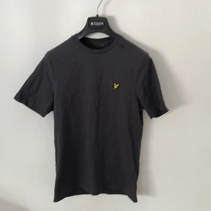 Svart t-shirt från Lyle & Scott - Svart t-shirt från Lyle & Scott med klassisk passform och korta ärmar. T-shirten har rund halsringning och den gula örnloggan broderad på bröstet. Tillverkad i mjuk bomull som är skön mot huden. Helt nytt skick oanvänd