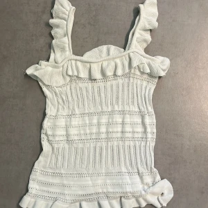 Vitt stickat linne från Dilvin - Supersöt vit stickad linnetopp från Dilvin med volangdetaljer på axelbanden och nederkanten. Toppen har ett luftigt, hålstickat mönster och är perfekt nu inför sommaren 💗. Stretchigt material som sitter snyggt och bekvämt.