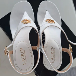 Urläckra Ralph Lauren sandaletter - Ursnygga Ralph Lauren sandaletter med 6 cm- blockklack som ger en elegant höjd till de smala remmarna och den guldfärgade metallglansen i de fantastiska Westcott II-sandalerna från Lauren by Ralph Lauren.                                                   Tyvärr, med mina breda fötter brukar jag ofta satsa på fel skor 😉. Skorna är i nyskick. 