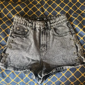 Grå jeansshorts med kedjedetaljer XS - Snygga grå denimshorts från FB Sister i högmidjad modell. Shortsen har coola kedjedetaljer och snörning i sidorna, klassiska fickor fram och bak. 