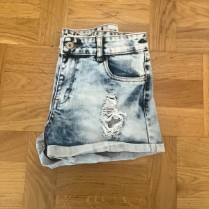 Ljusblå slitna jeansshorts - Snygga ljusblå jeansshorts med slitna detaljer och upprullade benslut. Shortsen har klassisk femficksmodell, bälteshällor och en cool tvättad look. Perfekta för varma dagar när du vill ha en avslappnad och trendig stil.