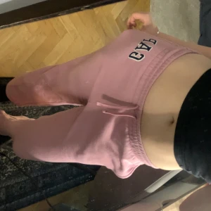 Rosa mjukisbyxor från GAP - Säljer ett par rosa mjukisbyxor från GAP med broderad logga framtill. Byxorna har låg midja, resår och snörning i midjan för skön passform. Tillverkade i mjukt bomullsmaterial, perfekta för chill dagar hemma. Inget fel på de helt nya men säljer för de inte kom till användning + det var för korta i benen på mig är 165 men har långa ben:) kostar 340 helt nya