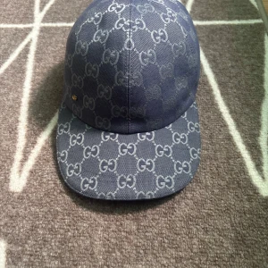 Gucci keps Blå - Snygg blå keps från Gucci i storlek S, täckt av det klassiska GG-monogrammet i ljusare blått. Kepsen är tillverkad i bomull och har en böjd skärm. Perfekt för dig som vill sticka ut med en exklusiv accessoar.