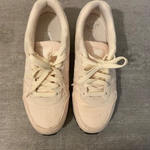 Beige Nike sneakers i canvas - Snygga beige Nike sneakers i canvas med klassisk vit swoosh på sidan. Skorna har rund tå, platt sula och snörning framtill. Perfekta för dig som gillar en clean och stilren look till vardags. Lätta och bekväma att bära.