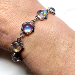 Armband med regnbågsskimrande stenar - Unikt handgjort armband med runda, regnbågsskimrande glasstenar infattade i silverfärgade länkar. Stenarna har en cool holografisk effekt som skiftar i blått, lila och gult beroende på ljuset. Armbandet har ett hjärtformat T-lås som detalj. Perfekt för dig som gillar att sticka ut, är nickel fritt.