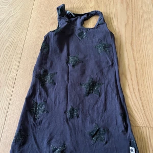 Svart linnetopp med glittriga stjärnor - Cool svart linnetopp från H&M Kids med glittriga svarta stjärnor över hela plagget. Modellen är ärmlös med brottarrygg och tillverkad i mjuk bomull, perfekt för en avslappnad och trendig look.