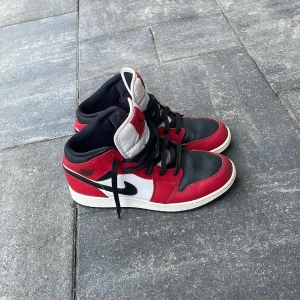 Nike Air Jordan 1 Chicago sneakers - Säljer ett par äkta Nike Air Jordan 1 i Chicago-färg. Skorna har svart, rött och vitt skinn, klassisk svart swoosh och högt skaft. Tungan är vit med röd patch och svart Jumpman-logga. Perfekta för dig som vill sticka ut med en tidlös streetwear-look. 