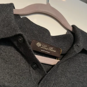 Mörkgrå pikétröja i kashmir från Loro Piana - Exklusiv mörkgrå långärmad pikétröja från Loro Piana i mjuk kashmir. Klassisk krage med knappar framtill och diskret, stilren look. Perfekt för dig som gillar lyxiga och tidlösa plagg med premiumkänsla. Perfekt för lite kyligare sommar kvällar. Pris kan diskuteras!