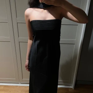 Svart långklänning med halterneck - Säljer en helt ny svart satinklänning med scarf (polyester) från australiensiska Runaway the Label. Köpte i fel färg ,prislappen sitter kvar och den är helt oanvänd. Tjockt, lyxigt material med silikonband i bysten så den sitter på plats. Slutar precis ovanpå fötterna (jag är 170 cm). Nypris ca 2900 kr inkl. frakt, tull och moms. Säljes till angivet pris. 