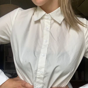 Vit klassisk skjorta med knappar - Säljer en stilren vit skjorta med klassisk krage och knäppning framtill. Skjortan har lång ärm och är tillverkad i ett mjukt bomullstyg. Perfekt för en clean och enkel look.