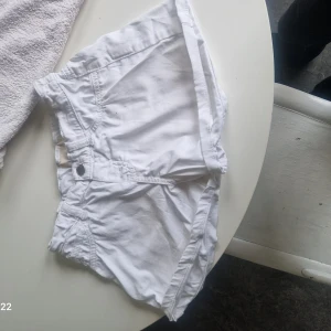 Vita shorts low waist - Snygga vita shorts med klassisk knappstängning och fickor framtill. De har en enkel design med uppvikta benslut och är perfekta för varma dagar. Materialet känns lätt och passar bra till sommarens outfits.