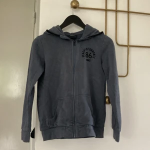 Blå hoodie från Peak Performance XS - Mörkblå hoodie från Peak Performance i storlek XS. Tröjan har dragkedja framtill, huva och två fickor. Tryck med 'Peak Performance 86' på bröstet. Perfekt för chill dagar eller när du vill ha en sportig look.