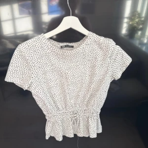 Prickig topp från Zara - Supersöt vit topp från Zara med svarta prickar, korta ärmar. Midjan har en snygg snörning som ger en fin form. 