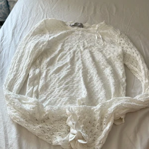 Vit spetsblus med knyt från Dilvin - Superfin vit blus från Dilvin i spets med lång ärm och snygg knytning i midjan. Blusen har ett romantiskt mönster och är perfekt för dig som gillar detaljer. Lätt och luftig känsla, passar till jeans eller kjol för en trendig look.