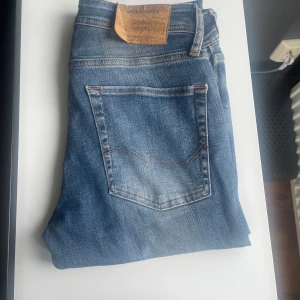 Jack & Jones jeans slim Glenn - Snygga blå slim fit jeans från Jack & Jones med slitna detaljer och klassisk femficksdesign. Jeansen har lagom slitningar. Jeans är i strl W28/L30. Ny pris 899kr. Hör av dig vid mer frågor!