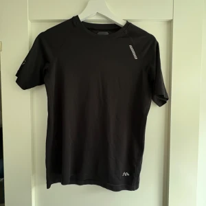 Svart träningst-shirt från Karhu - Svart t-shirt från Karhu med diskret logga på bröstet och ärmen. Tillverkad i ett lätt och stretchigt material som passar perfekt för träning. Klassisk rund hals och korta ärmar ger en clean och sportig look.