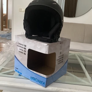 Svart skidhjälm från KYROB - Säljer en svart skid- och snowboardhjälm från KYROBA. Hjälmen har en stilren design med justerbart hakspänne och vadderade öronskydd för extra komfort. Perfekt för dig som vill ha både säkerhet och stil i backen. Storlek 54-56 cm