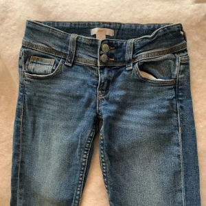 Blå jeans från Gina Tricot, stl 140 - Snygga blå jeans från Gina Tricot i storlek 140. Klassisk femficksmodell med dubbla knappar i midjan och justerbar resår på insidan. Jeansen har utsvegda ben och snygga slitningar för en cool look.