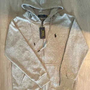 Grå hoodie från Polo Ralph Lauren - En helt ny med QR kod och allt tröja ifrån Ralph Lauren. Tröjan är aldrig använd så inga defekter!       Priset kan diskuteras!!