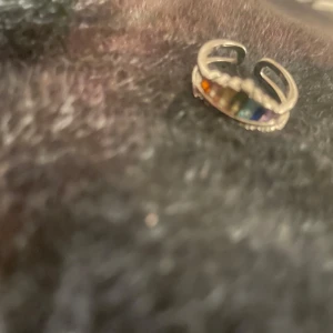 Regnbågsfärgad silverring justerbar - Unik justerbar ring i silverfärgad metall med raka stavar i regnbågens färger framtill. Ringen har öppet band och dekorativa detaljer längs kanten. Perfekt statement piece för dig som gillar färg och vill sticka ut.