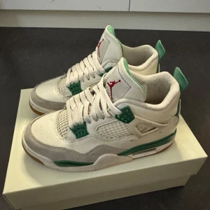 Nike SB Air Jordan 4 Pine Green - Nike SB Air Jordan 4 Pine Green med vit och grön färg, röda detaljer på tungan och klassisk meshpanel. Skorna har snörning, platt sula och är tillverkade i skinn och mocka. Perfekta för dig som gillar streetstyle och unika sneakers. Storlek 37,5 kvitto och original kartong medföljer. Bra skick och går att tvätta för att fräscha upp dem. (De är otvättade på bilderna)