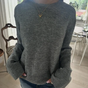 Grå stickad tröja med långa ärmar - Mysig grå stickad tröja med rund halsringning och långa ärmar. Tröjan har breda ribbade muddar vid ärmslut och nederkant, vilket ger en avslappnad och trendig look. Perfekt att styla med jeans eller kjol för en chill vibe❤️❤️