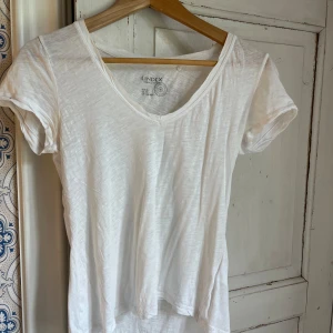 Vit v-ringad t-shirt från Lindex - En klassisk vit t-shirt från Lindex med v-ringning och korta ärmar. Tillverkad i tunn, mjuk bomull som känns skön mot huden. Perfekt basic-plagg med enkel och stilren look, passar till allt och är lätt att matcha.