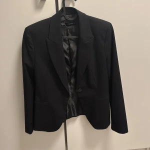 Svart kavaj från Zara, storlek 36 - Stilren svart kavaj från Zara i klassisk modell med en knapp framtill och spetsiga slag. Fodrad insida i glansigt tyg och två fickor framtill. Perfekt för en clean och snygg look. Passar dig som gillar tidlös stil.