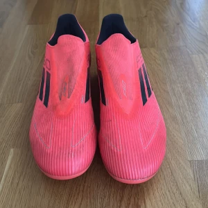 Adidas F50 rosa fotbollsskor - Säljer ett par Adidas F50 fotbollsskor i en riktigt snygg rosa färg med svarta detaljer och silverlogga bak. Skorna har en strömlinjeformad design utan snörning och är gjorda i syntetmaterial för bästa känsla på planen.