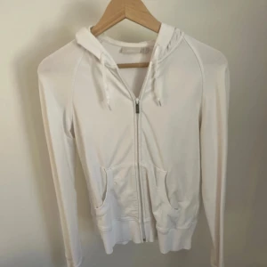 Vit hoodie med dragkedja från Mexx - Vit hoodie från Mexx i mjuk bomull med dragkedja framtill, huva med snörning och två fickor. Långärmad och enkel design som passar perfekt till jeans eller leggings. Snygg och clean look för dig som gillar basic streetstyle.