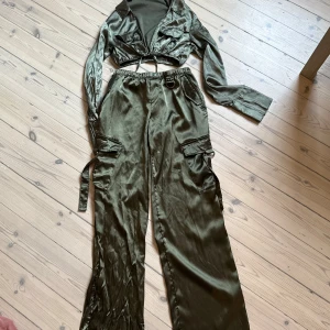 Olivgrönt set från Divided H&M - Snygga olivgröna cargopants med matchande långärmad crop top till  från H&M Divided i glansigt material. Byxorna har flera fickor på sidorna, bred resår i midjan och raka ben med loose fit. Perfekta för en cool streetstyle-look.