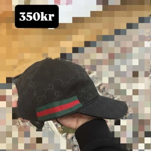Svart GG keps snygg - Snygg svart keps från  med klassiskt GG-monogram över hela kepsen. På sidan finns en grön och röd rand som ger den en lyxig vibe. Kepsen har böjd skärm och justerbar rem bak. Perfekt för dig som vill sticka ut med en ikonisk accessoar.