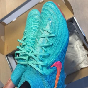 Nike Phantom Luna II Elite FG turkosa - Nike Phantom Luna II Elite LV8 FG i en fräsch turkos färg. Skorna har gräsdubbar! Helt nya och oanvända med tag hängande kvar.