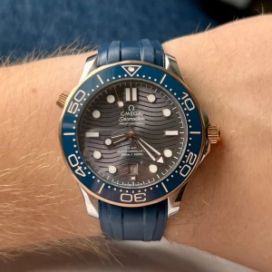 Omega Seamaster Diver 300M blå/guld - Omega Seamaster Professional Diver 300M med blå gummiband och blå urtavla med vågmönster. Boetten är i rostfritt stål och guld, vridbar bezel i blått och guld, samt tydliga index och datumfönster. Automatisk urverk syns genom glasbaksidan. Riktigt snygg och sportig dykarklocka.