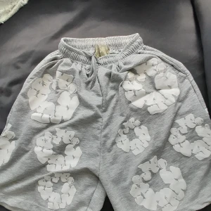 Grå shorts från Denim Tears med tryck - Säljer ett par grå shorts från Denim Tears med elastisk midja och snörning. Shortsen har unikt vitt blommönster tryckt över hela tyget och är tillverkade i mjuk bomull. Perfekta för chill dagar eller när du vill sticka ut lite extra.