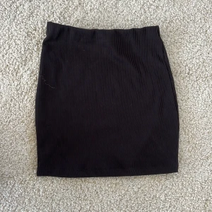 Svart ribbad kortkjol från Monki - Säljer en svart ribbad kortkjol från Monki i storlek XS. Kjolen har en tight passform och är tillverkad i ett stretchigt material